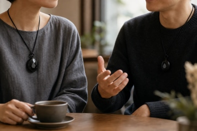 Two friends at a cafe table, both wearing a Fieldy pendant